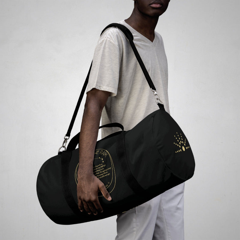 Person holding a black duffel bag with gold accents on a plain background