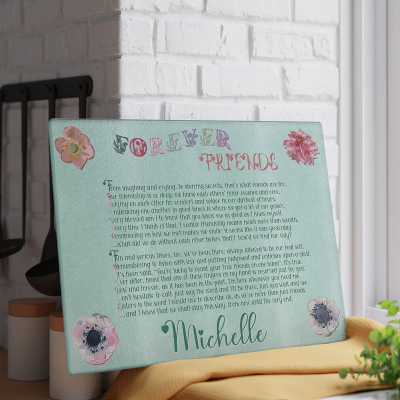Glass cutting board with acrostic poem spelling out 'Forever Friends' text and floral designs on a light blue background, placed against a white brick wall.