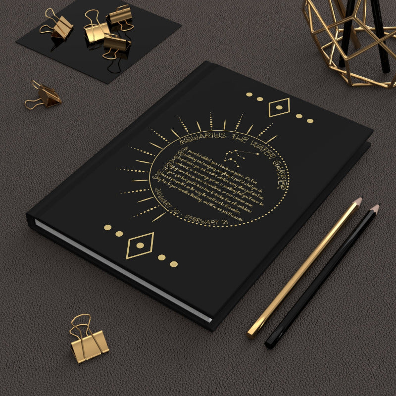 Black notebook with gold design on a dark surface with stationery items.