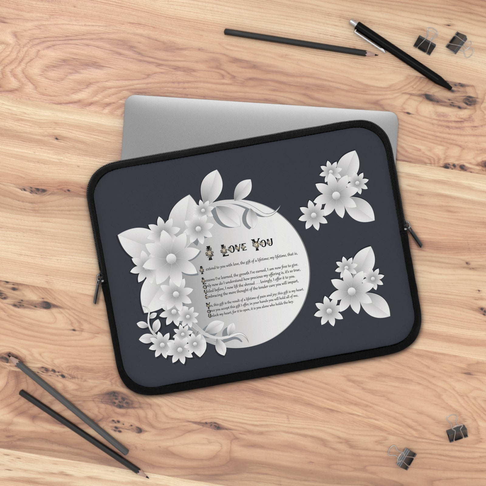 Laptop sleeve with floral design and acrostic poem spelling out 'I Love You' on a wooden surface with pens and pencils.