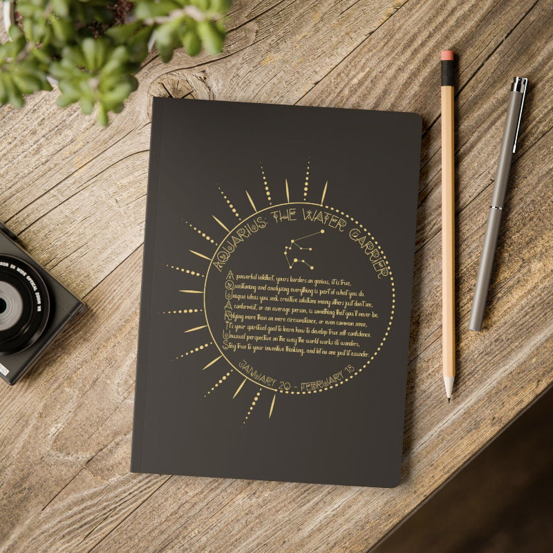 Black notebook with gold astrological design on a wooden surface with a pencil and pen.