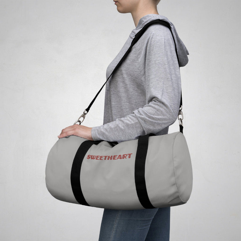 Person carrying a gray duffel bag with 'SWEETHEART' text on a plain background