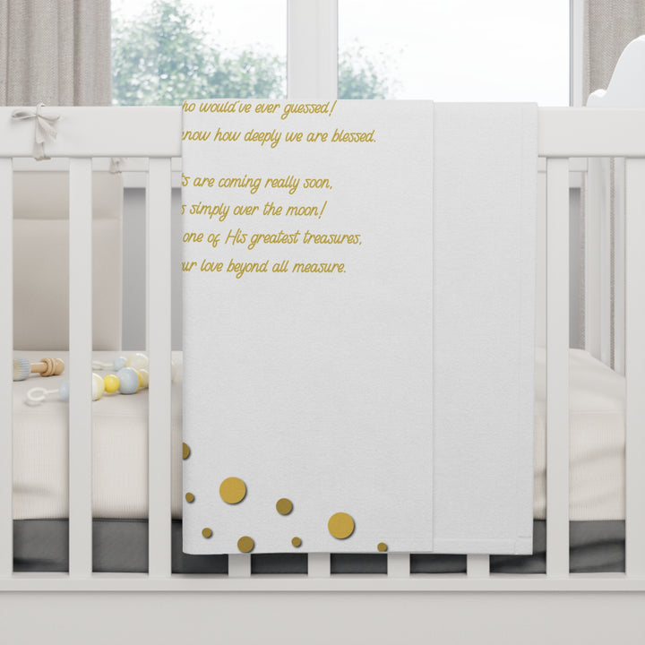 White crib with a white blanket featuring gold text and polka dots.