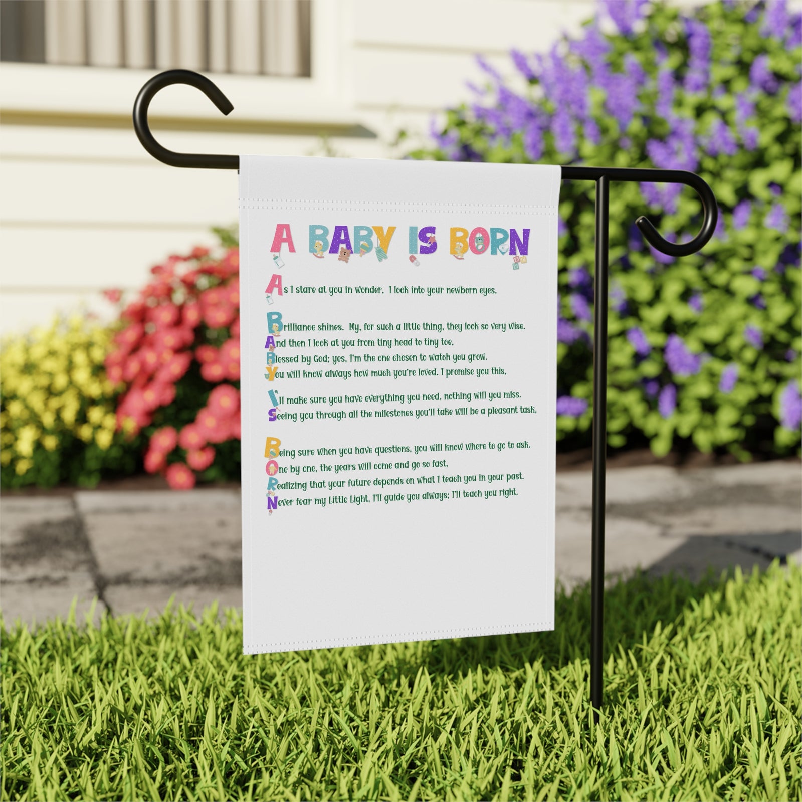 Garden sign with acrostic poem spelling out A Baby is Born on a grassy area with flowers in the background