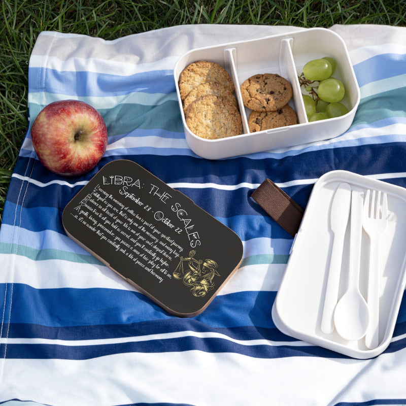 Picnic setup with a bento box with an acrostic poem spelling out Libra with apple, cookies, grapes, and a sign on a striped blanket outdoors.
